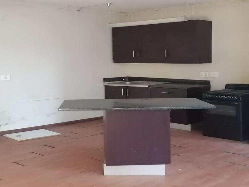 A compact kitchen featuring dark cabinetry, a central island, and a built-in stove, currently in need of cosmetic updates and floor repairs.