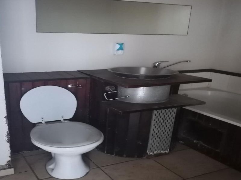 A dated bathroom featuring a vessel sink, toilet, and bathtub with worn cabinetry and visible wear on the wall base.