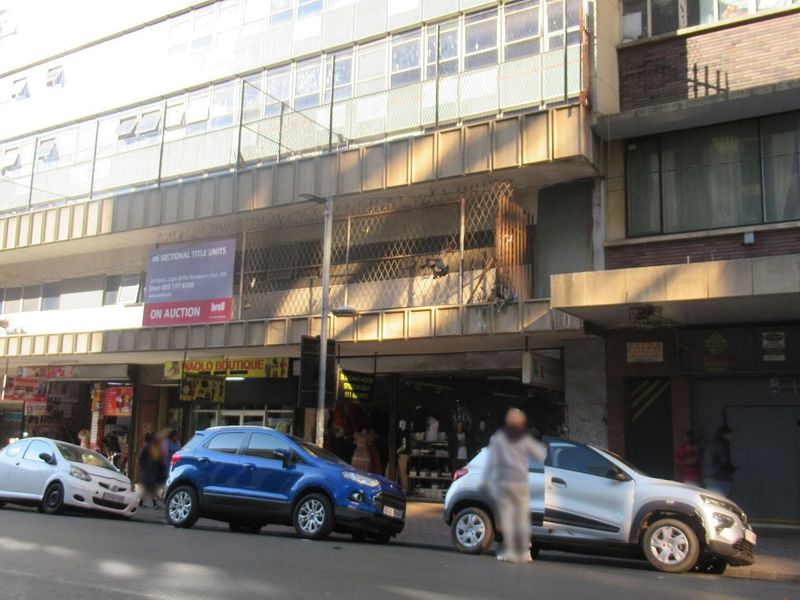 Street-level view of a multi-story apartment building featuring ground floor retail units and a weathered facade.
