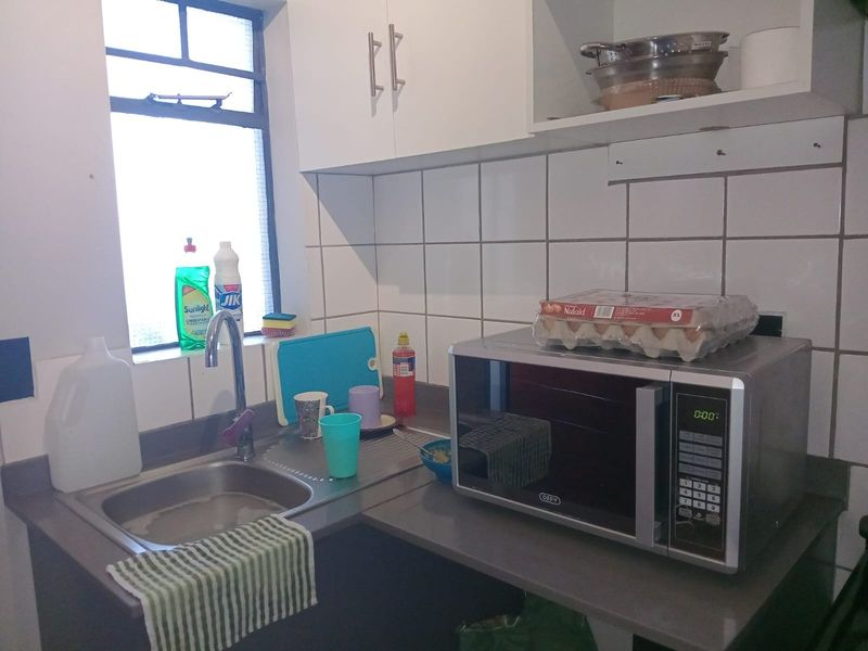 A compact kitchen area featuring a stainless steel sink, tiled splashback, and built-in cabinetry with laminate countertops.