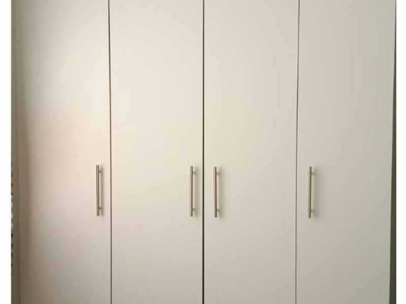 A clean, modern bedroom featuring a large white built-in wardrobe with integrated drawers and sleek metal handles.