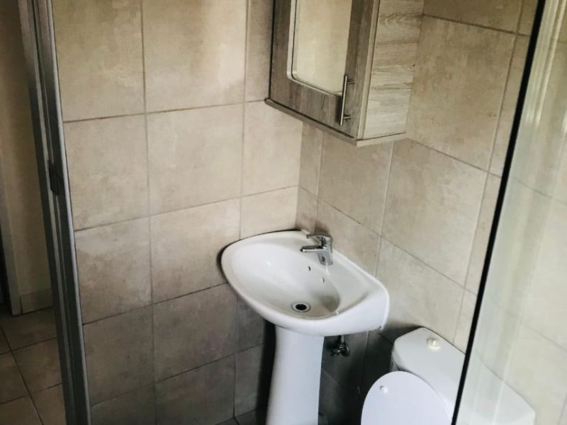 A compact bathroom featuring a pedestal basin, toilet, and wall-mounted medicine cabinet with neutral wall and floor tiling.