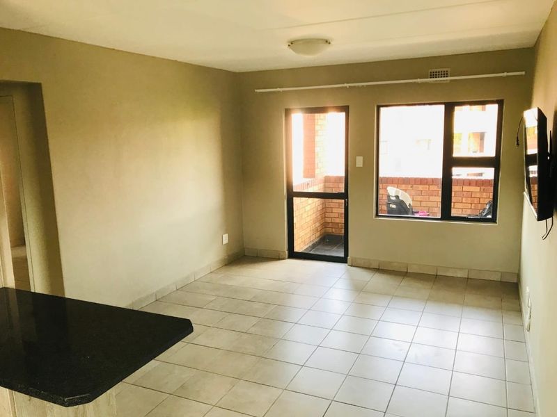 Open plan living area featuring neutral tiled flooring, a granite breakfast counter, and direct access to a private balcony through an aluminium door.