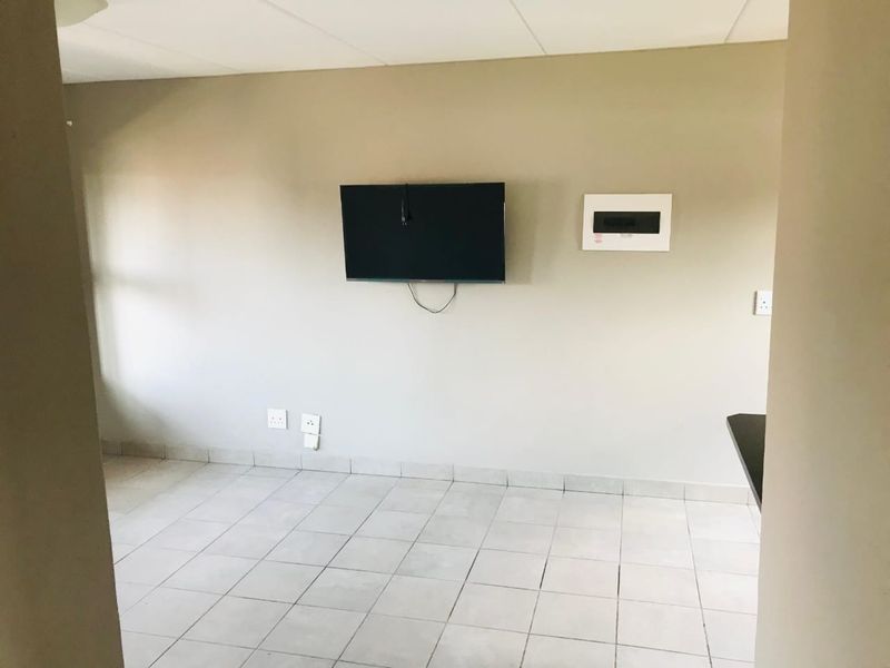 An empty living area featuring neutral tiled flooring, a wall-mounted television point, and a visible electrical distribution board.
