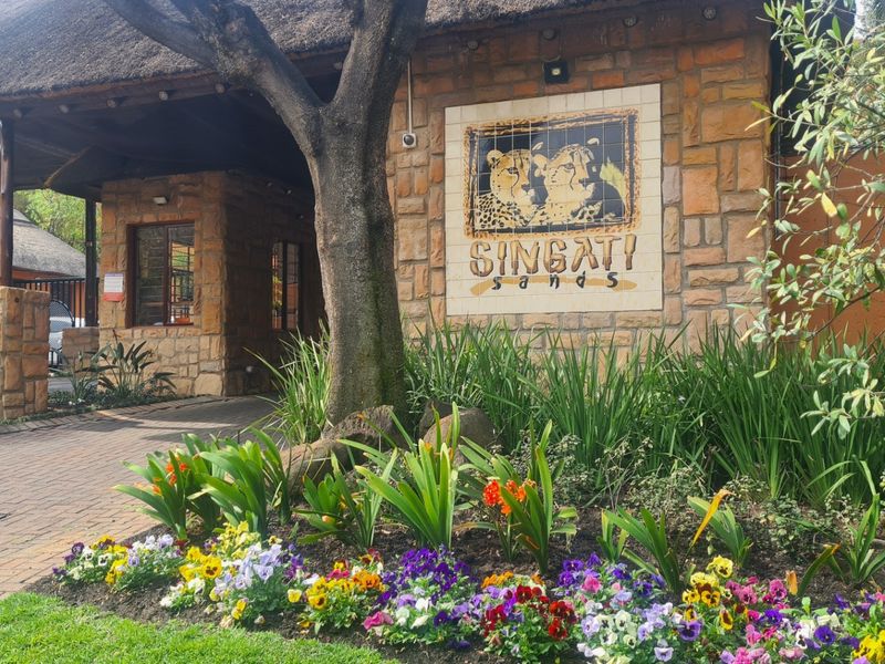 The entrance to Singati Sands featuring stone-clad walls, a traditional thatch roof, and well-maintained landscaped gardens with a paved driveway.