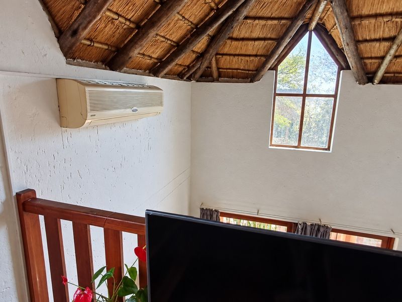 A living area featuring a high vaulted thatched ceiling with exposed timber rafters, a split-system air conditioner, and a timber balustrade overlooking the lower level.