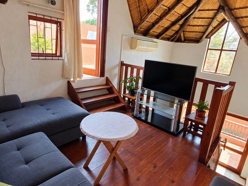 A cozy living area featuring a unique thatched roof, timber flooring, and a wooden staircase leading to a mezzanine level.