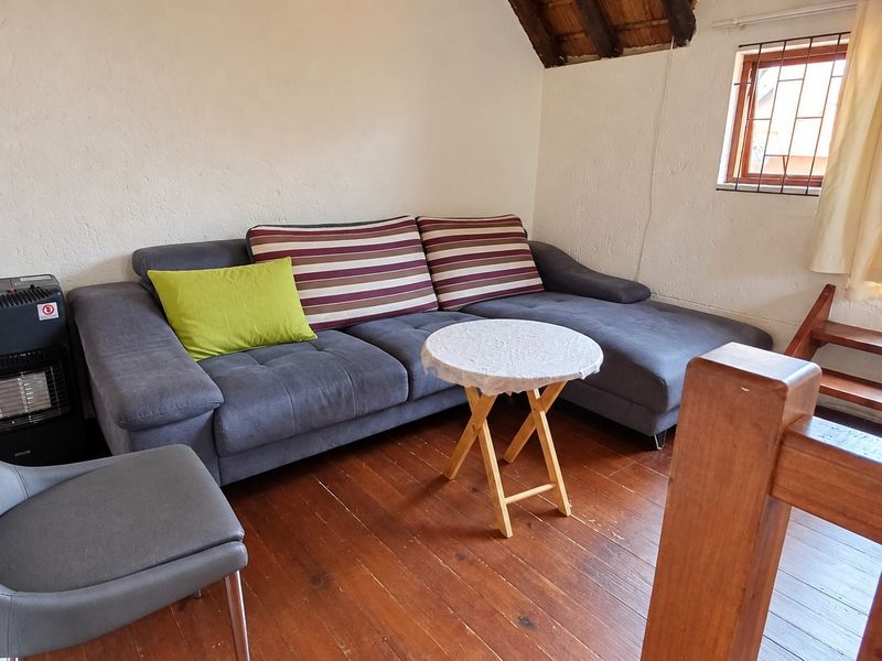 A cozy living area featuring exposed timber rafters, wooden flooring, and a window with security bars, offering a rustic and functional space.