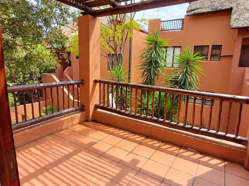 A spacious balcony featuring terracotta tiling, a timber pergola, and a wooden balustrade, offering an open outdoor area with views of the complex.