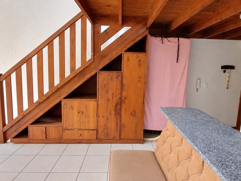 Open plan living area featuring a wooden staircase with integrated storage cabinetry, tiled flooring, and exposed timber ceiling beams.
