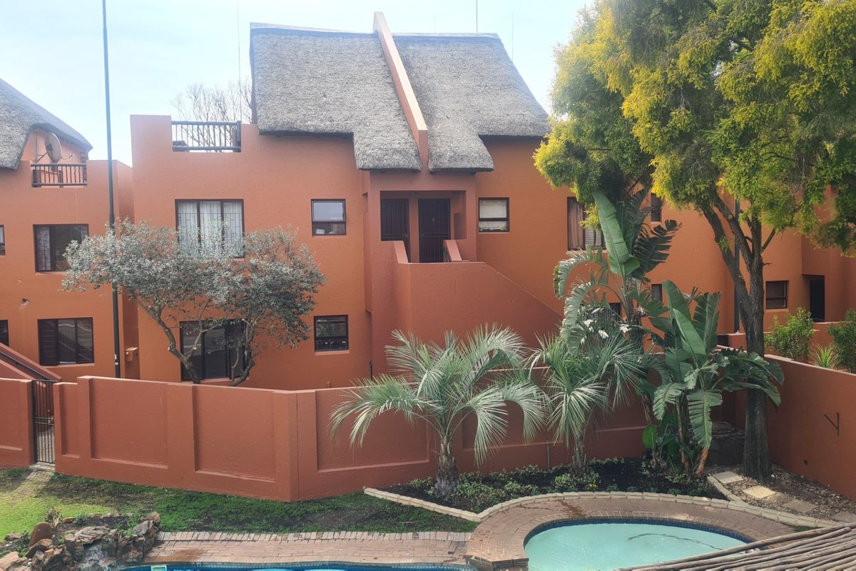 Rear view of a multi-story apartment complex featuring a thatched roof, private balcony, and a communal swimming pool area with landscaped garden.