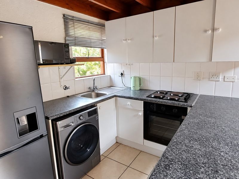 Compact kitchen featuring white cabinetry, dark laminate countertops, tiled backsplash, and exposed timber ceiling beams, equipped with a built-in oven and hob.