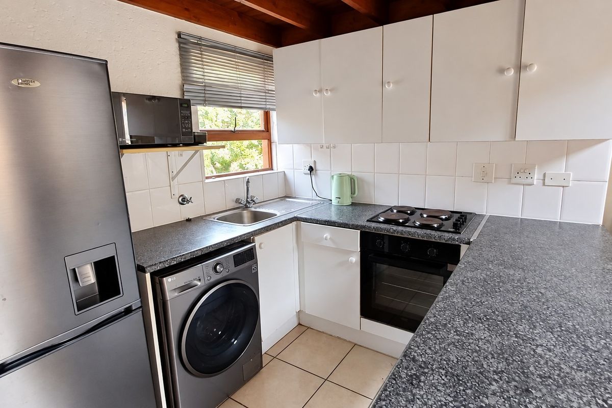 Compact kitchen featuring white cabinetry, dark laminate countertops, tiled backsplash, and exposed timber ceiling beams, equipped with a built-in oven and hob.
