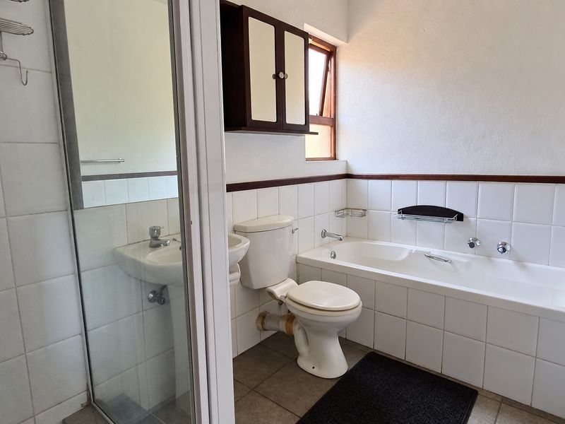 A functional bathroom featuring a separate shower enclosure, built-in bathtub, pedestal basin, and toilet with classic white wall tiling.