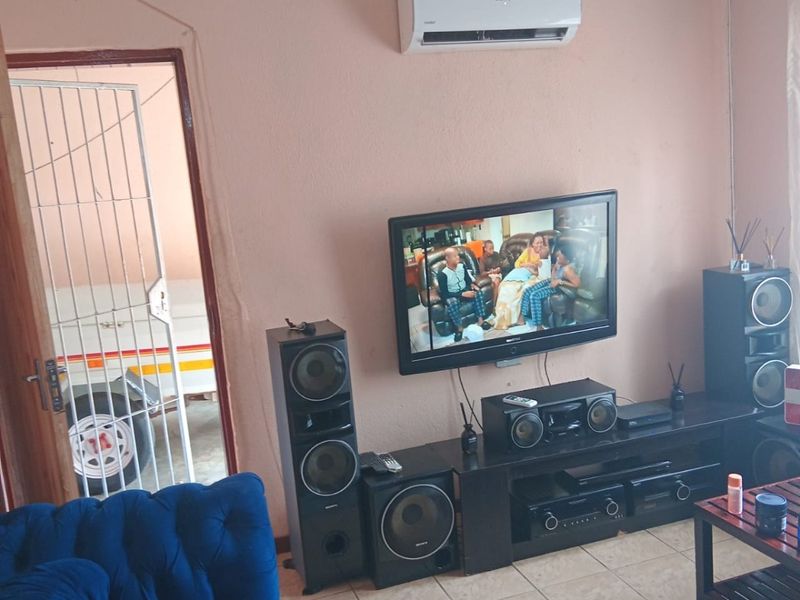 Living room featuring tiled flooring and a wall-mounted air conditioning unit, with direct access to an exterior area through a security gate.