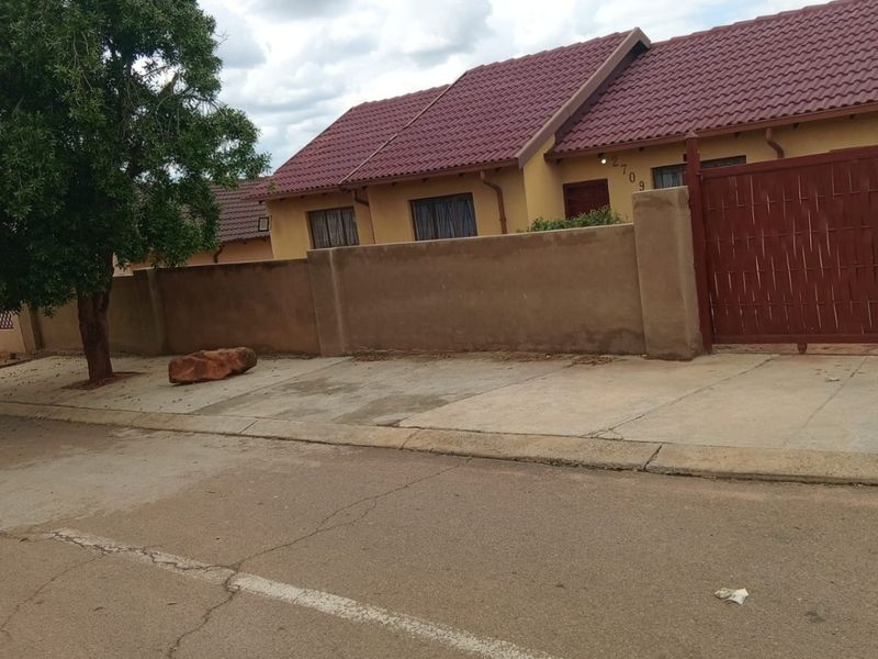 Front exterior view of a single-story house featuring a tiled roof, perimeter wall, and gated driveway access from the street.