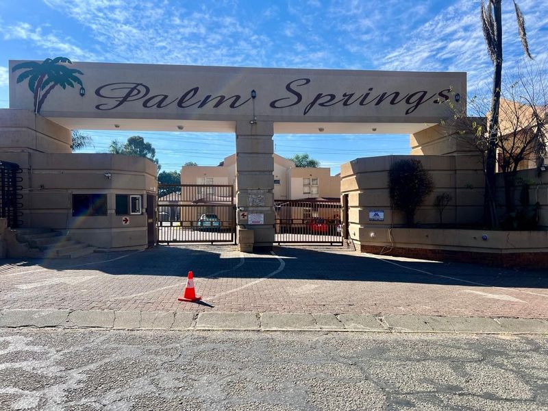 The main entrance gate and security access point for the Palm Springs townhouse complex, featuring paved driveway and gated security infrastructure.