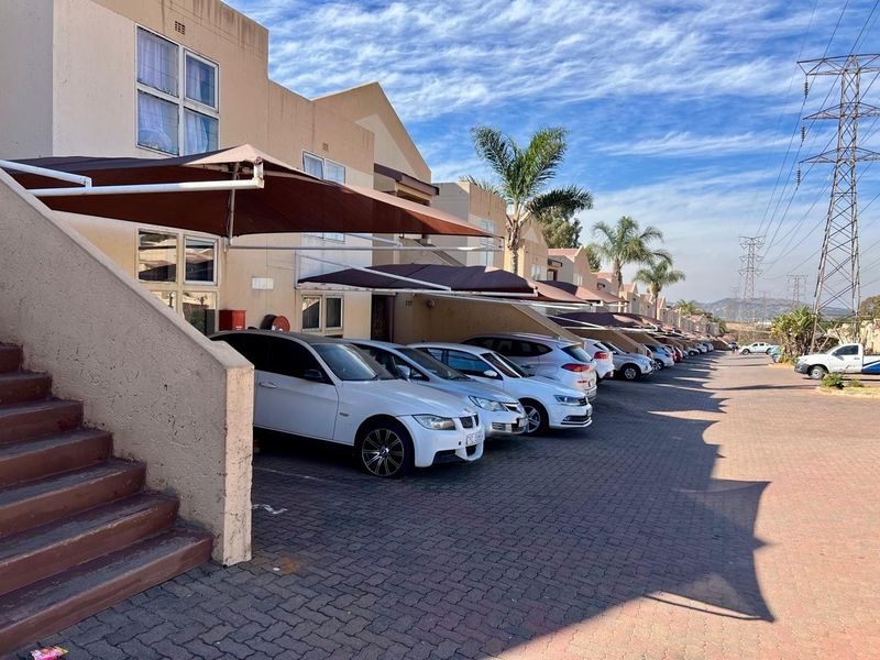 Exterior view of a townhouse complex featuring paved driveway parking with shade cloth carports and concrete stair access to units.