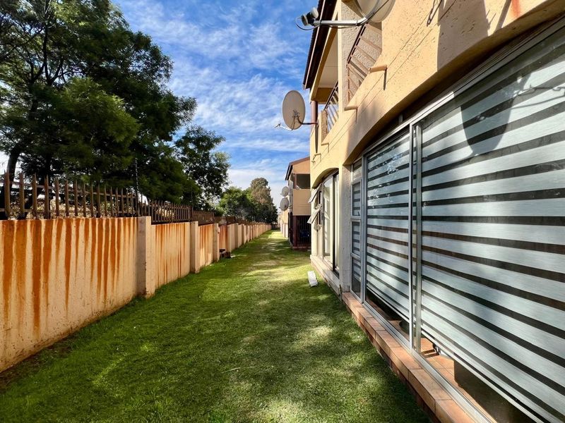 Rear exterior view of the townhouse featuring a lawn area, sliding glass doors, and a boundary wall with visible rust staining.
