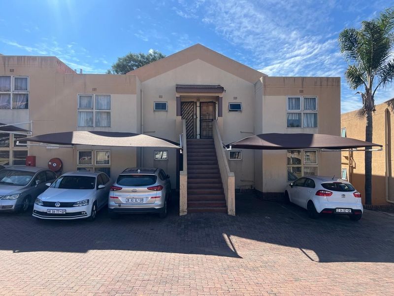 Front elevation of a townhouse complex featuring paved parking areas with shade cloth carports and an external staircase leading to upper-level units.