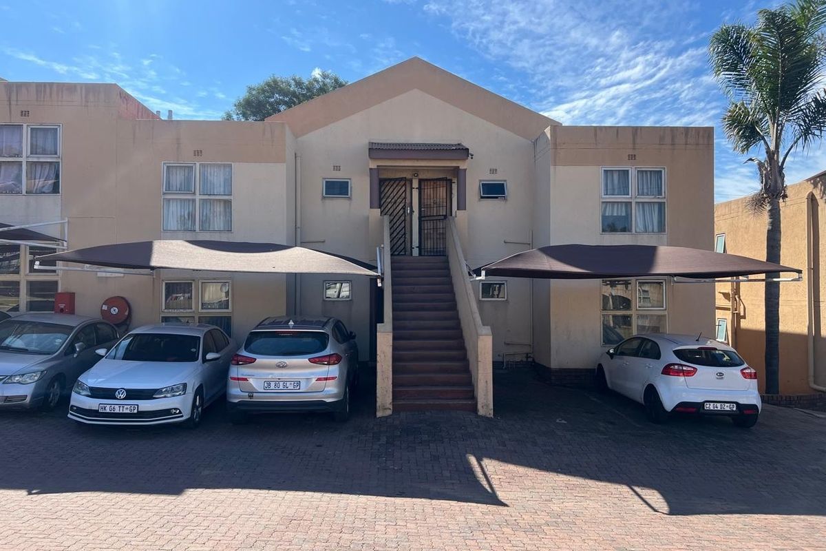 Front elevation of a townhouse complex featuring paved parking areas with shade cloth carports and an external staircase leading to upper-level units.