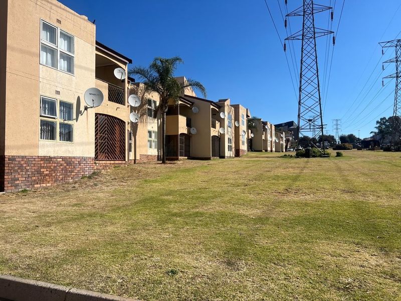 Exterior view of a townhouse complex featuring brick and plaster facades, private balconies, and security gates, situated near high voltage power lines.