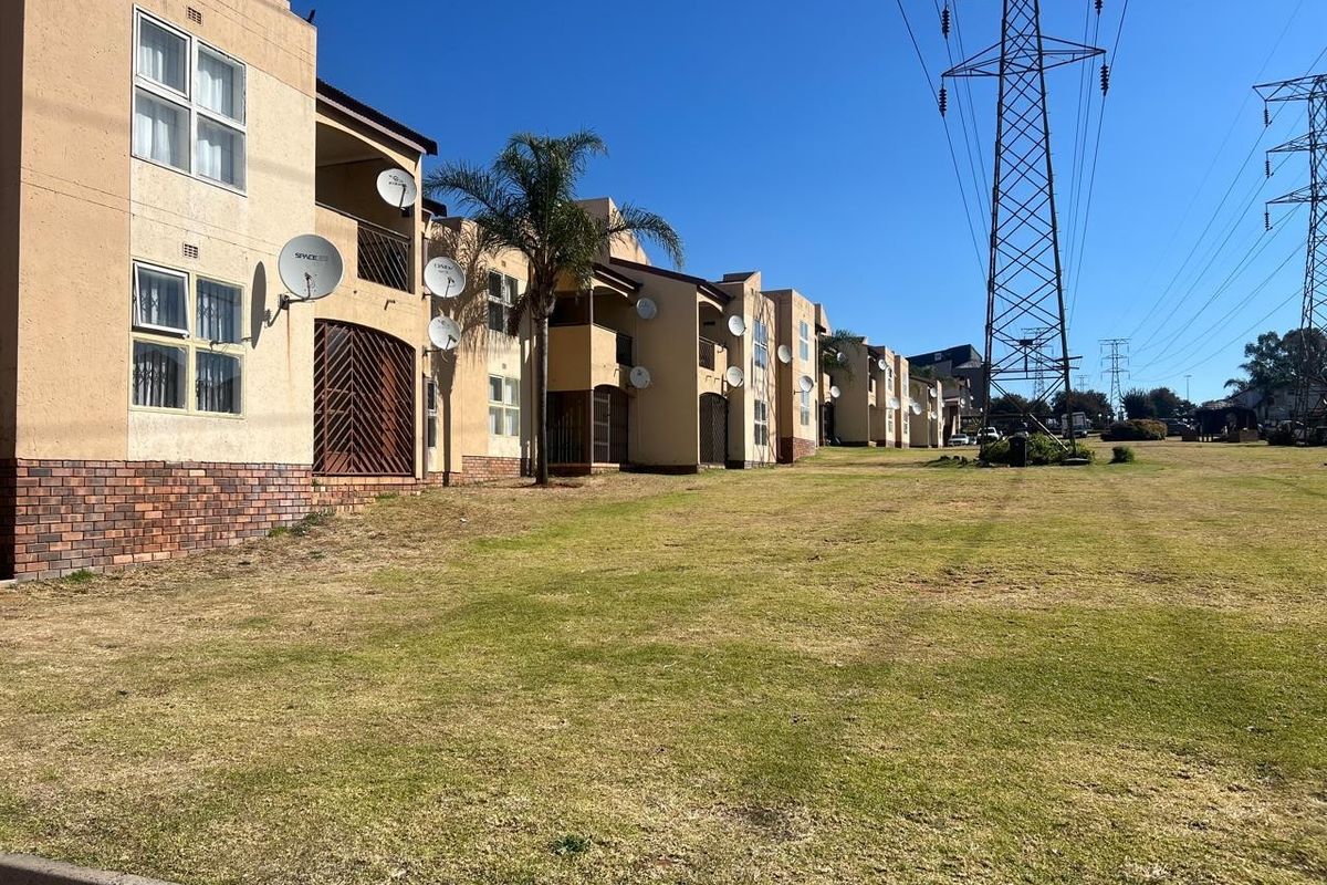 Exterior view of a townhouse complex featuring brick and plaster facades, private balconies, and security gates, situated near high voltage power lines.