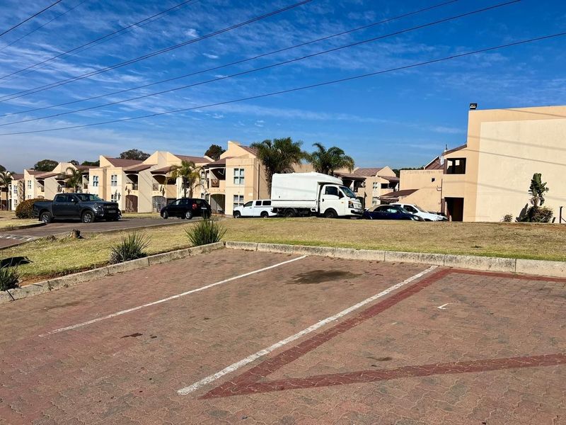 Exterior view of a townhouse complex featuring a paved parking area and multi-unit residential buildings with landscaped grounds.