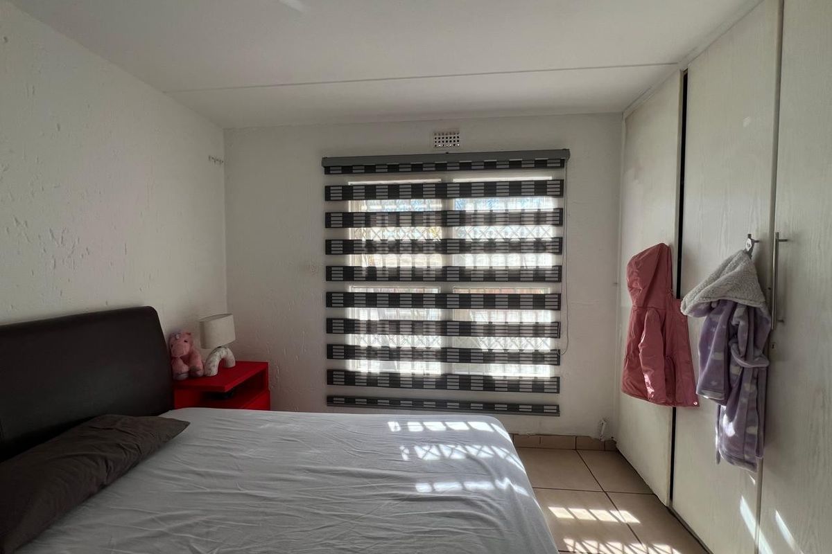 A functional bedroom featuring tiled flooring, built-in cupboards for storage, and modern window blinds providing adjustable natural light.