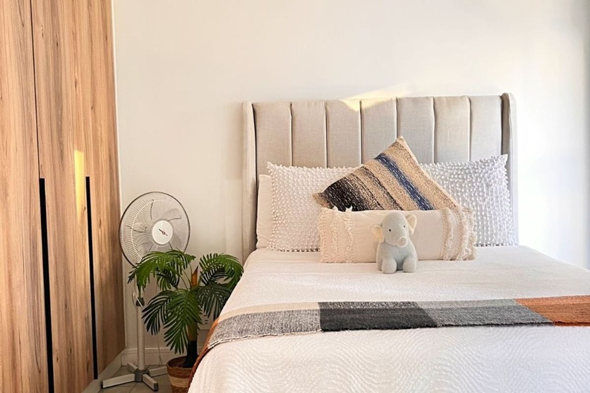 A well-maintained bedroom featuring modern wood-finish built-in wardrobes, neutral tiled flooring, and a contemporary pendant light fixture.