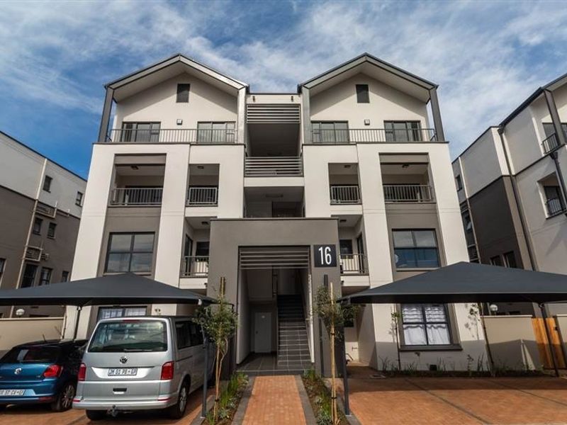 Modern multi-story apartment complex featuring a paved driveway, covered parking bays, and private balconies for each unit.