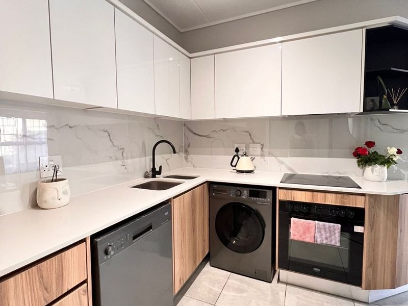 Modern kitchen featuring high-gloss white upper cabinets, wood-grain lower cabinetry, marble-effect splashback, and integrated appliances including an oven and hob.
