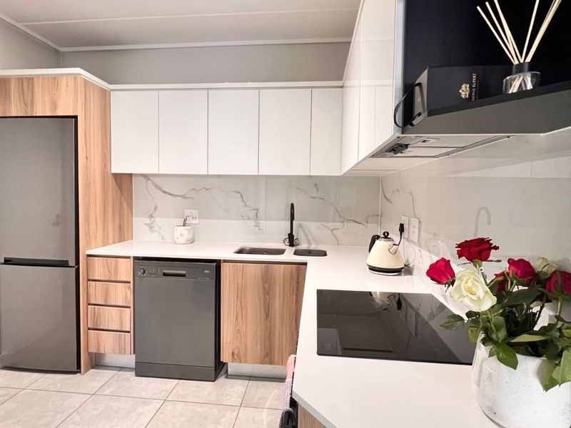 Modern kitchen featuring sleek two-tone cabinetry, stone countertops, marble-look splashback, integrated appliances, and contemporary track lighting.
