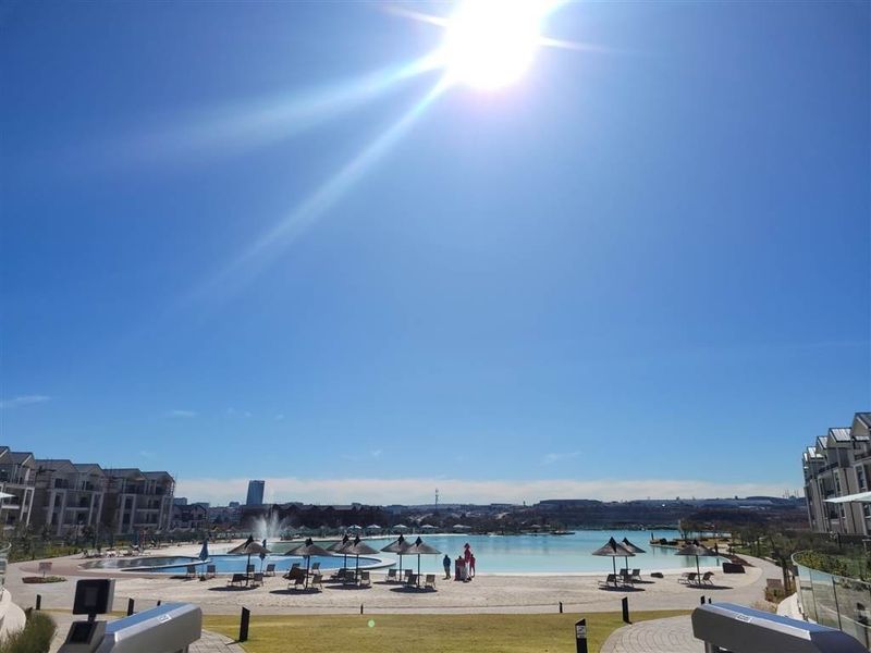 A scenic view of a large communal swimming pool area with landscaped surroundings and paved pathways within the apartment complex.