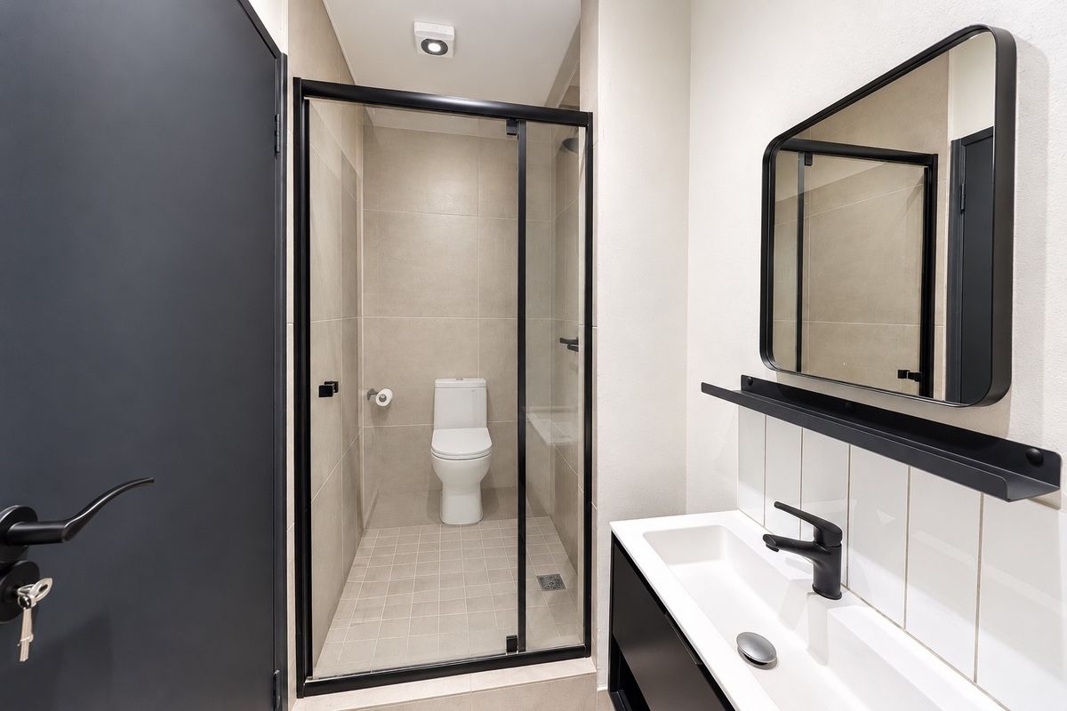 Modern bathroom featuring a glass-enclosed shower, sleek black tapware, a vanity basin, and neutral wall and floor tiling.