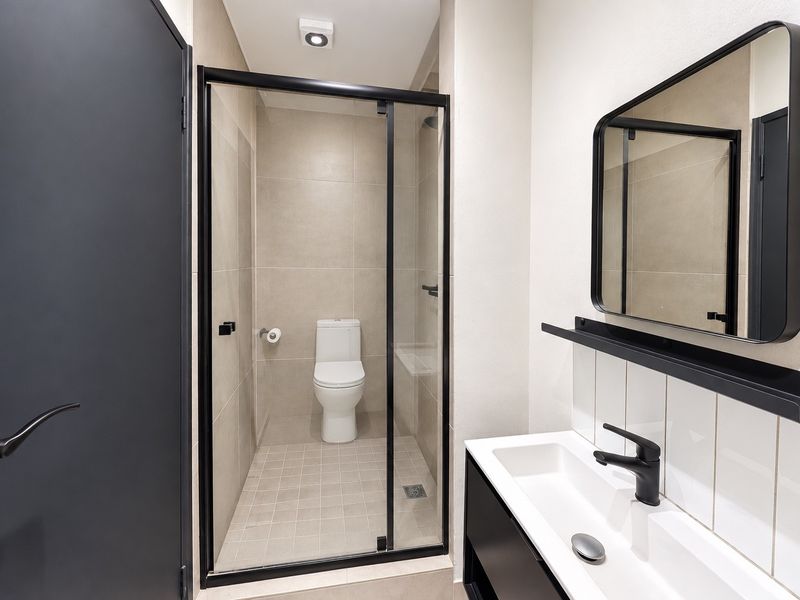 Modern bathroom featuring a glass-enclosed shower, sleek black tapware, a vanity basin, and neutral wall and floor tiling.