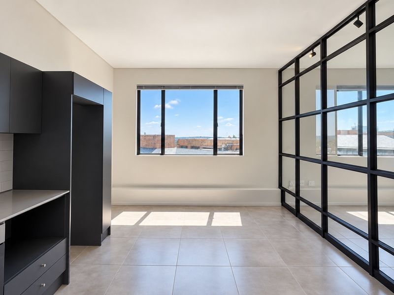 Modern open-plan kitchen area featuring sleek dark cabinetry, integrated appliances, tiled flooring, and a stylish black metal-framed glass partition wall.
