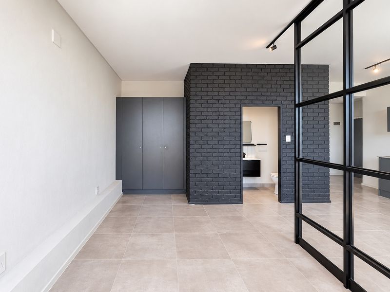 Modern open-plan living area featuring a striking black exposed brick wall, sleek built-in cupboards, and a contemporary black metal framed glass partition.