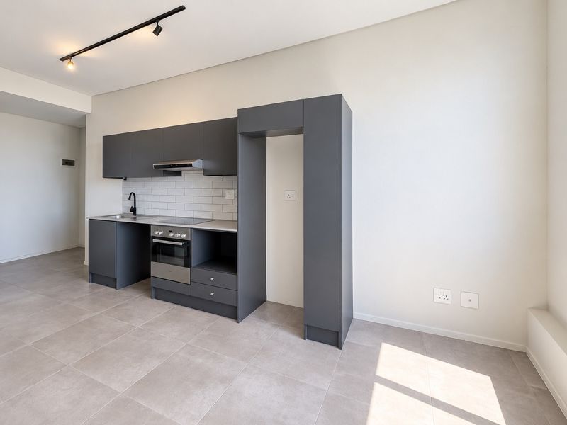 Modern open-plan kitchen featuring sleek dark grey cabinetry, integrated oven and hob, subway tile backsplash, and neutral tiled flooring in a bright, contemporary space.