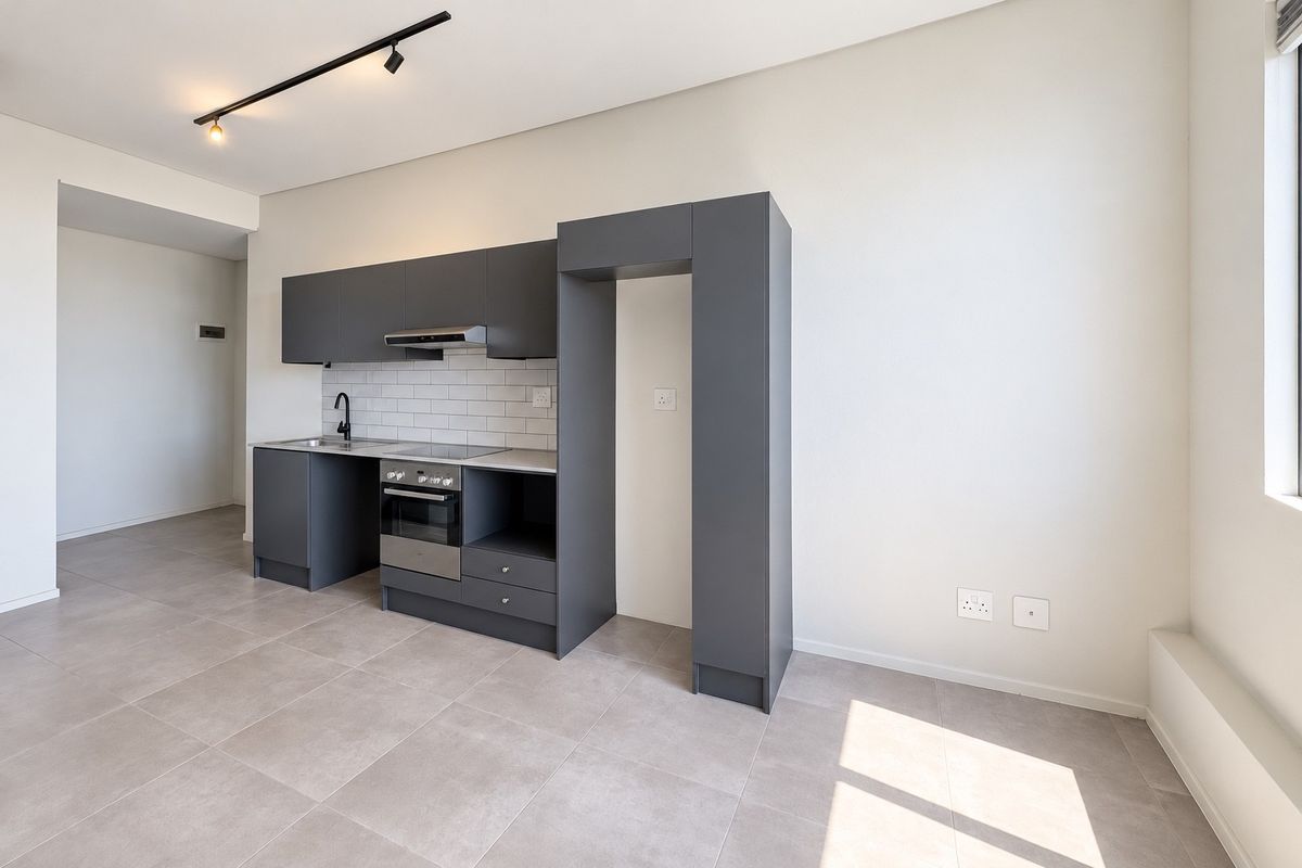 Modern open-plan kitchen featuring sleek dark grey cabinetry, integrated oven and hob, subway tile backsplash, and neutral tiled flooring in a bright, contemporary space.