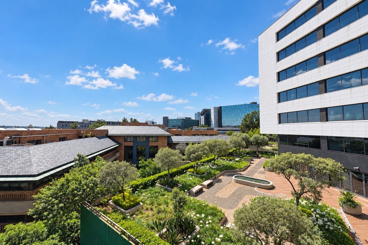 An elevated view of a well-maintained landscaped courtyard garden featuring paved walkways, a central water feature, and surrounding modern building architecture.