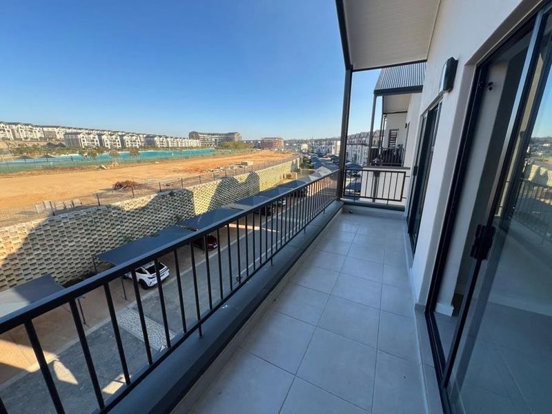 A modern, tiled balcony featuring a metal balustrade and sliding glass door access, offering an elevated view of the surrounding estate.