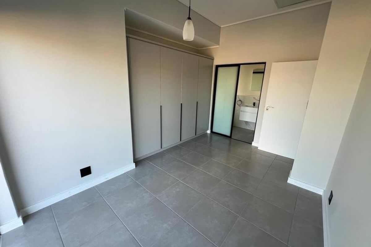A modern, empty bedroom featuring neutral grey tiled flooring, floor-to-ceiling built-in cupboards, and direct access to an en-suite bathroom.