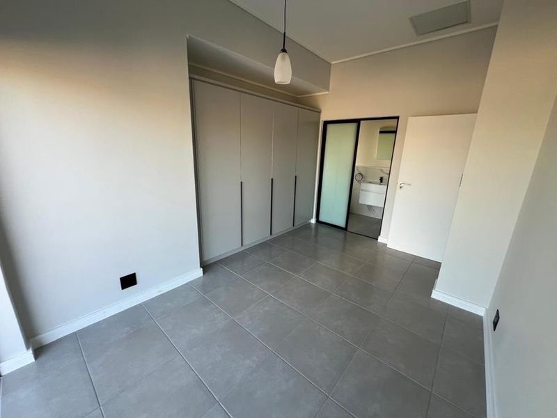 A modern, empty bedroom featuring neutral grey tiled flooring, floor-to-ceiling built-in cupboards, and direct access to an en-suite bathroom.