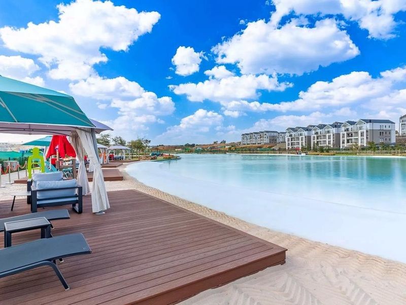 A well-maintained communal pool area featuring a sandy beach entry, timber decking, and views of the surrounding apartment complex.