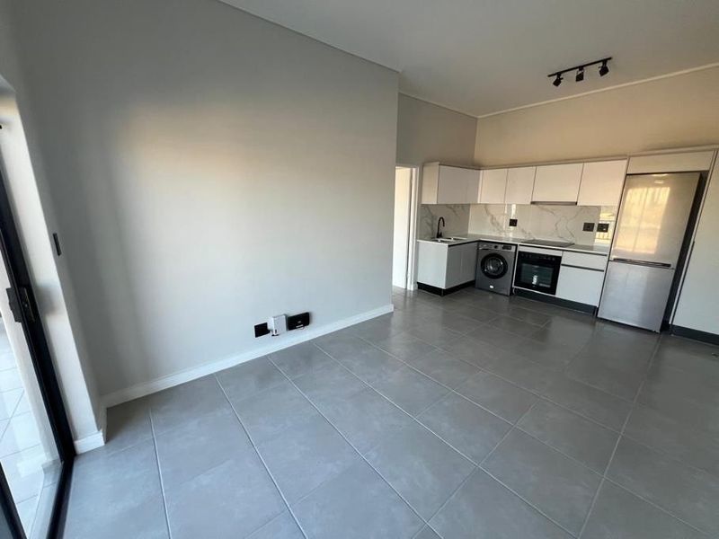 Modern open-plan living area featuring sleek cabinetry, integrated kitchen appliances, large format floor tiles, and direct access to an outdoor space via sliding doors.