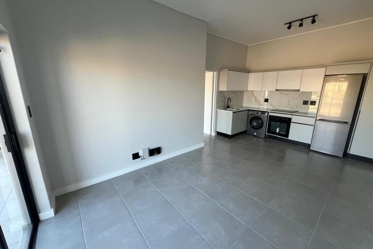 Modern open-plan living area featuring sleek cabinetry, integrated kitchen appliances, large format floor tiles, and direct access to an outdoor space via sliding doors.