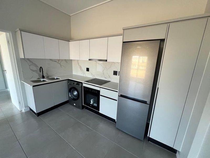 Modern kitchen featuring sleek white cabinetry, marble-look splashback, stone countertops, integrated appliances, and contemporary black fixtures.