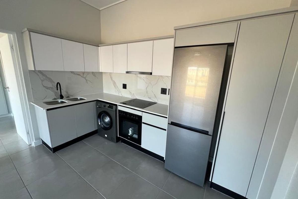 Modern kitchen featuring sleek white cabinetry, marble-look splashback, stone countertops, integrated appliances, and contemporary black fixtures.