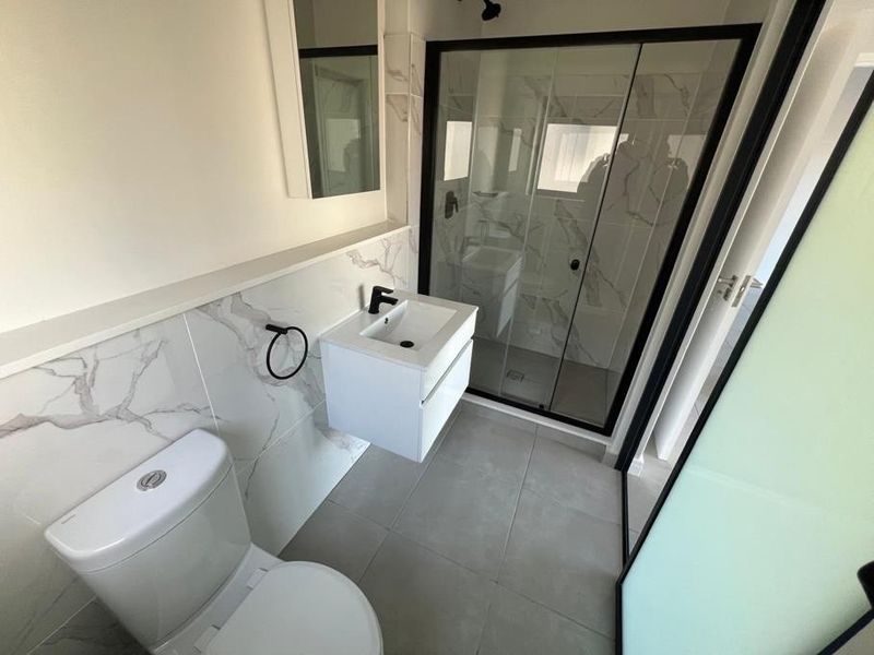 Modern bathroom featuring a wall-mounted vanity, walk-in shower with black-framed glass screen, and elegant marble-look wall tiling.